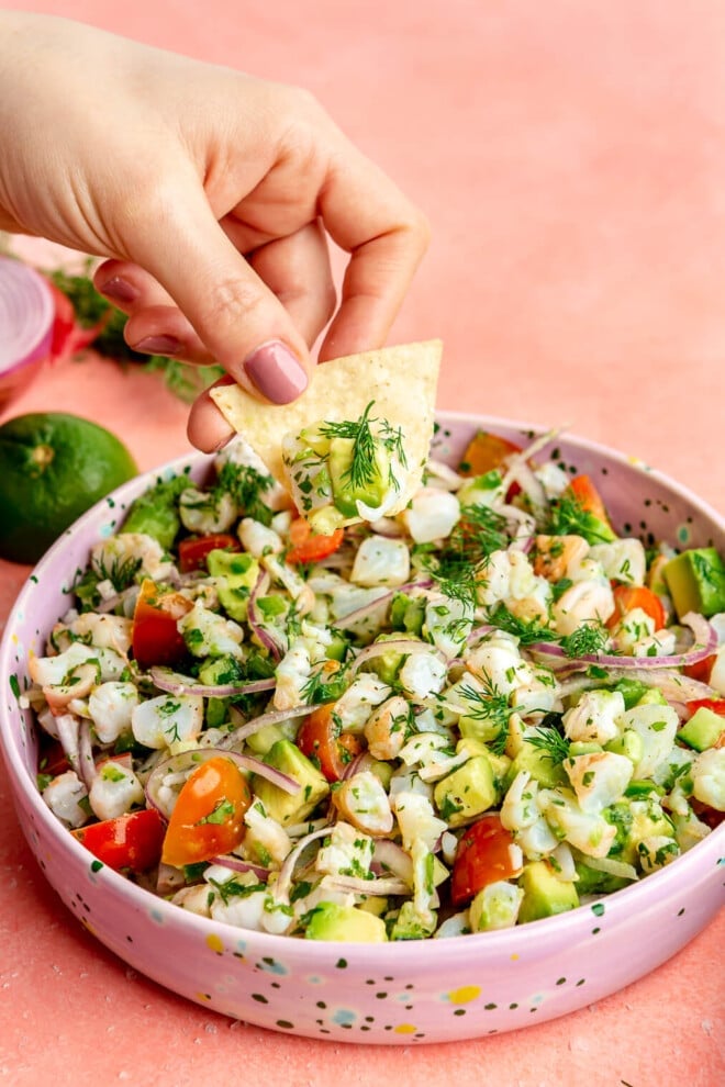 A person using a tortilla chip to scoop up shrimp ceviche from a bowl.