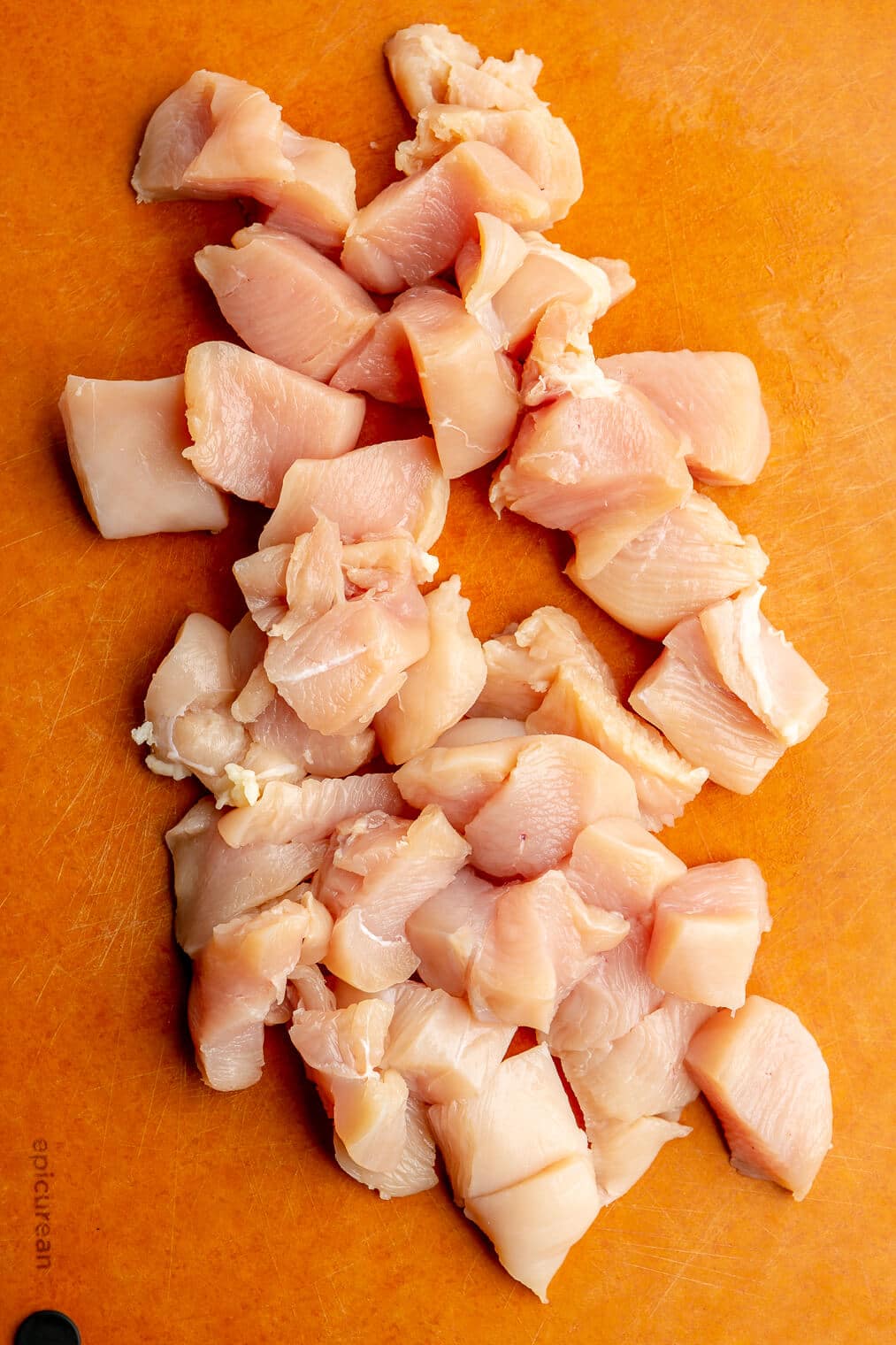 Cut chicken pieces (for chicken and veggie kabobs) on a cutting board.