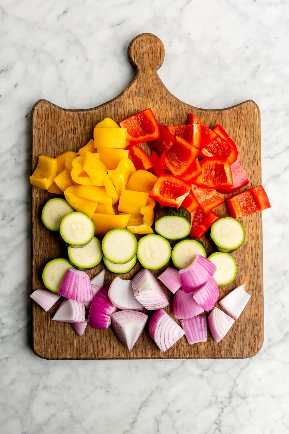 Cut veggies for chicken and veggie kabobs on a wooden cutting board.
