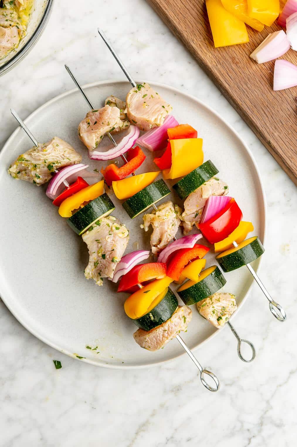 Three raw chicken and veggie kabobs on a plate.