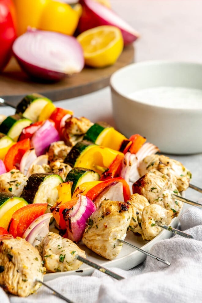 Side view of 6 chicken and veggie kabobs on a large plate.