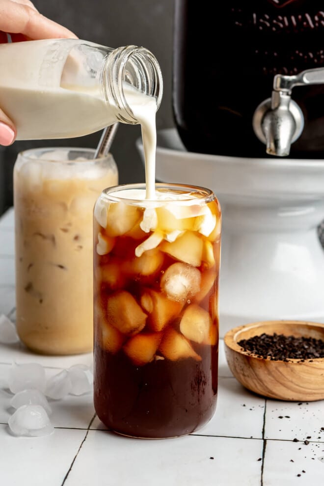 A person pouring heavy cream into a glass of iced cold brew.