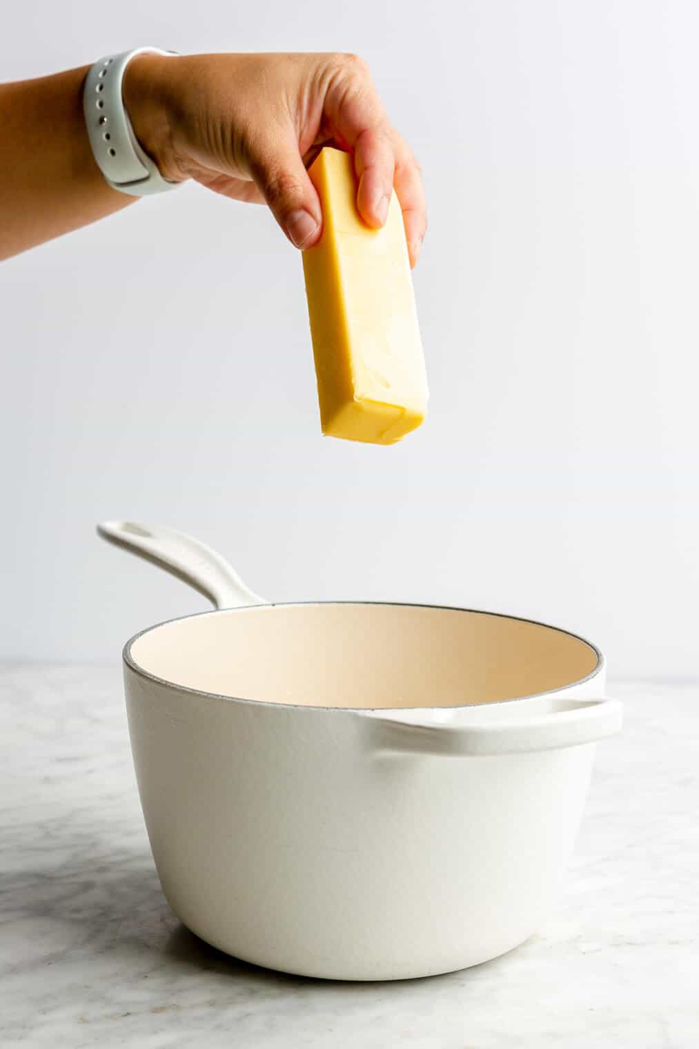 A person holding a stick of butter over a white pot.