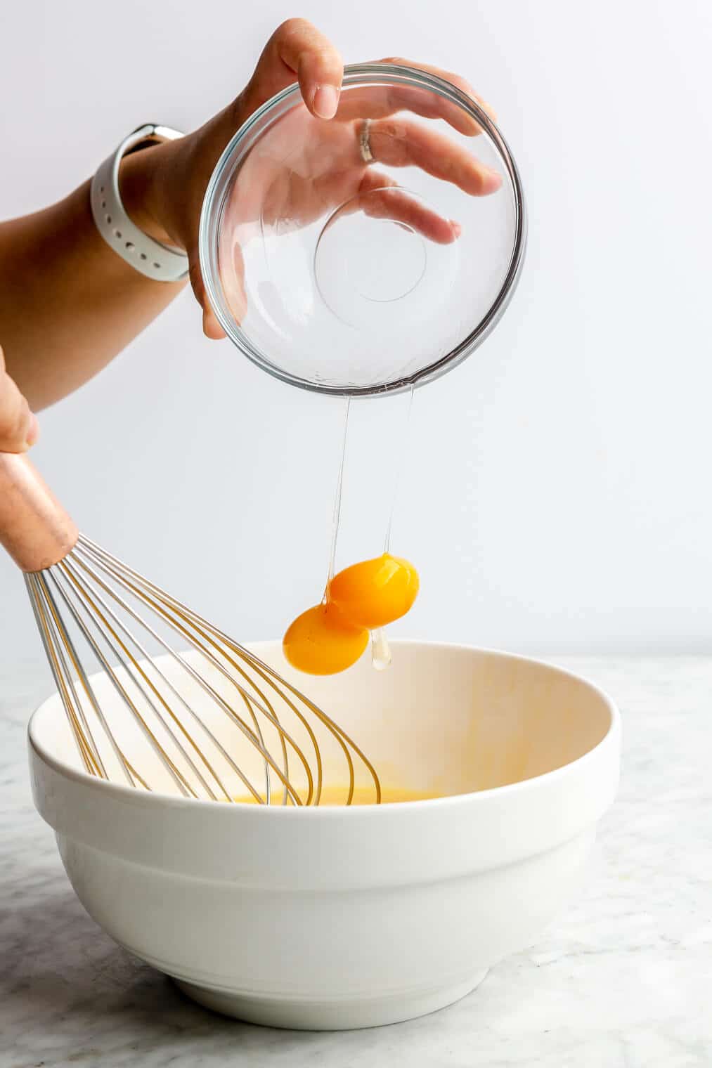 A person adding two egg yolks into a large white bowl.