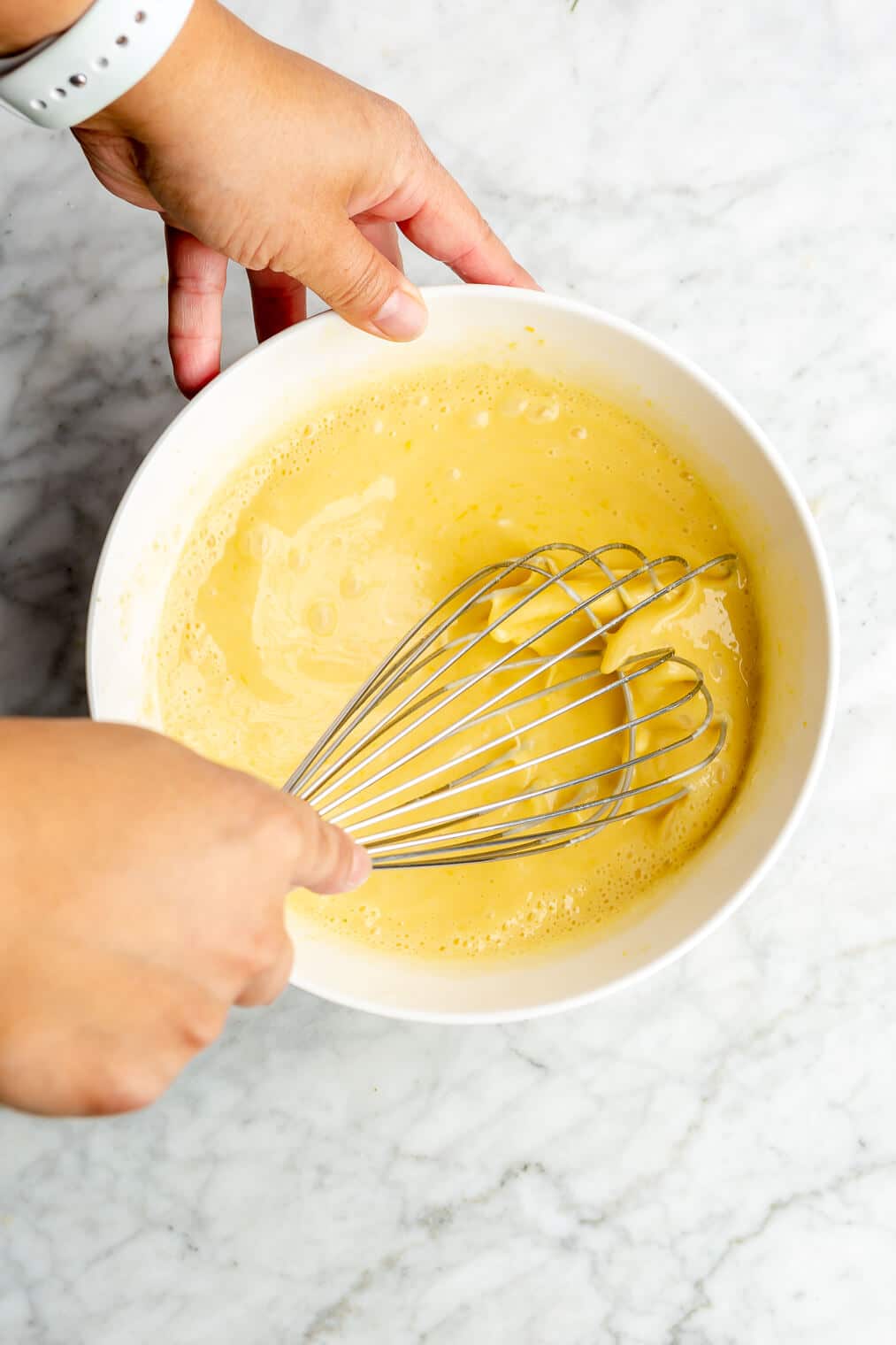 A person whisking together a yellow liquid in the process of making lemon curd.