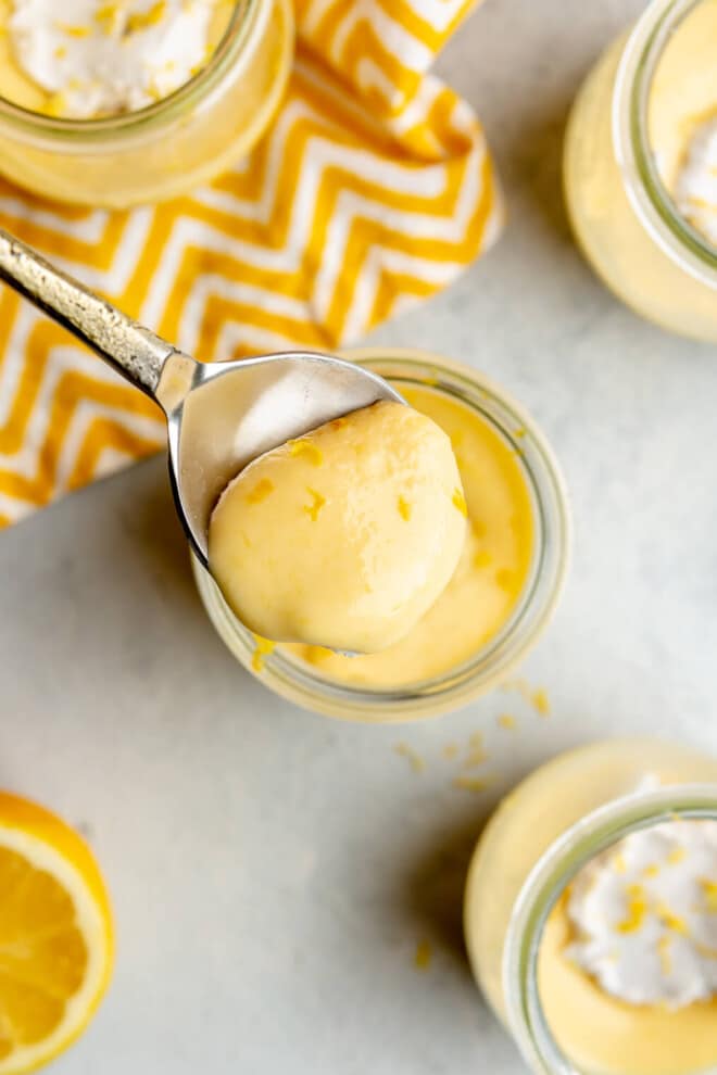 A person holding a spoon of lemon curd over several jars of lemon curd.