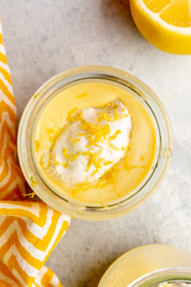 A small jar of lemon curd topped with coconut whipped cream and lemon zest.