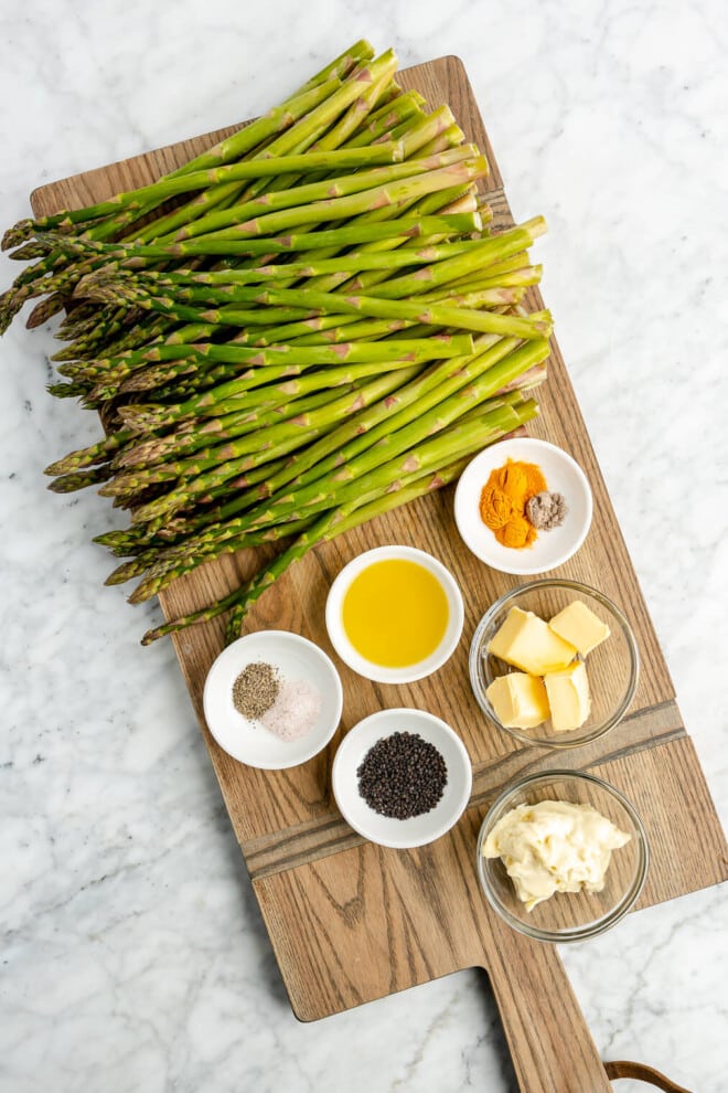 All of the ingredients for roasted asparagus with lemon cardamom sauce on a wooden cutting board.