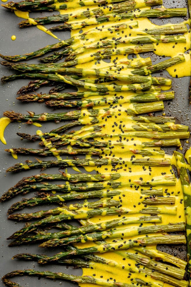 A close up of roasted asparagus topped with a bright yellow lemon cardamom sauce and black sesame seeds.
