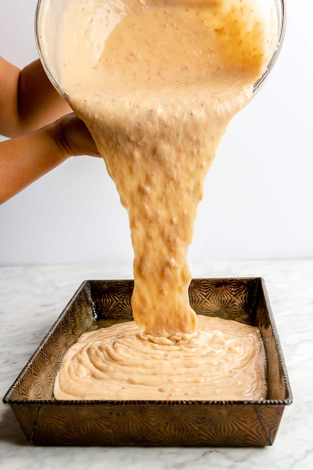 Strawberry cake batter being poured into a cake pan.