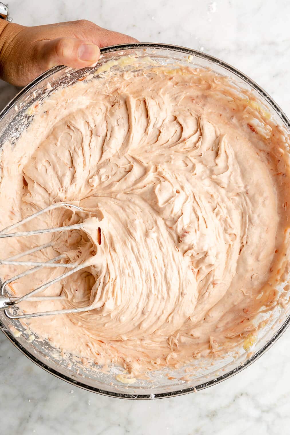 Strawberry cream cheese frosting in a large glass bowl being mixed with a hand mixer.