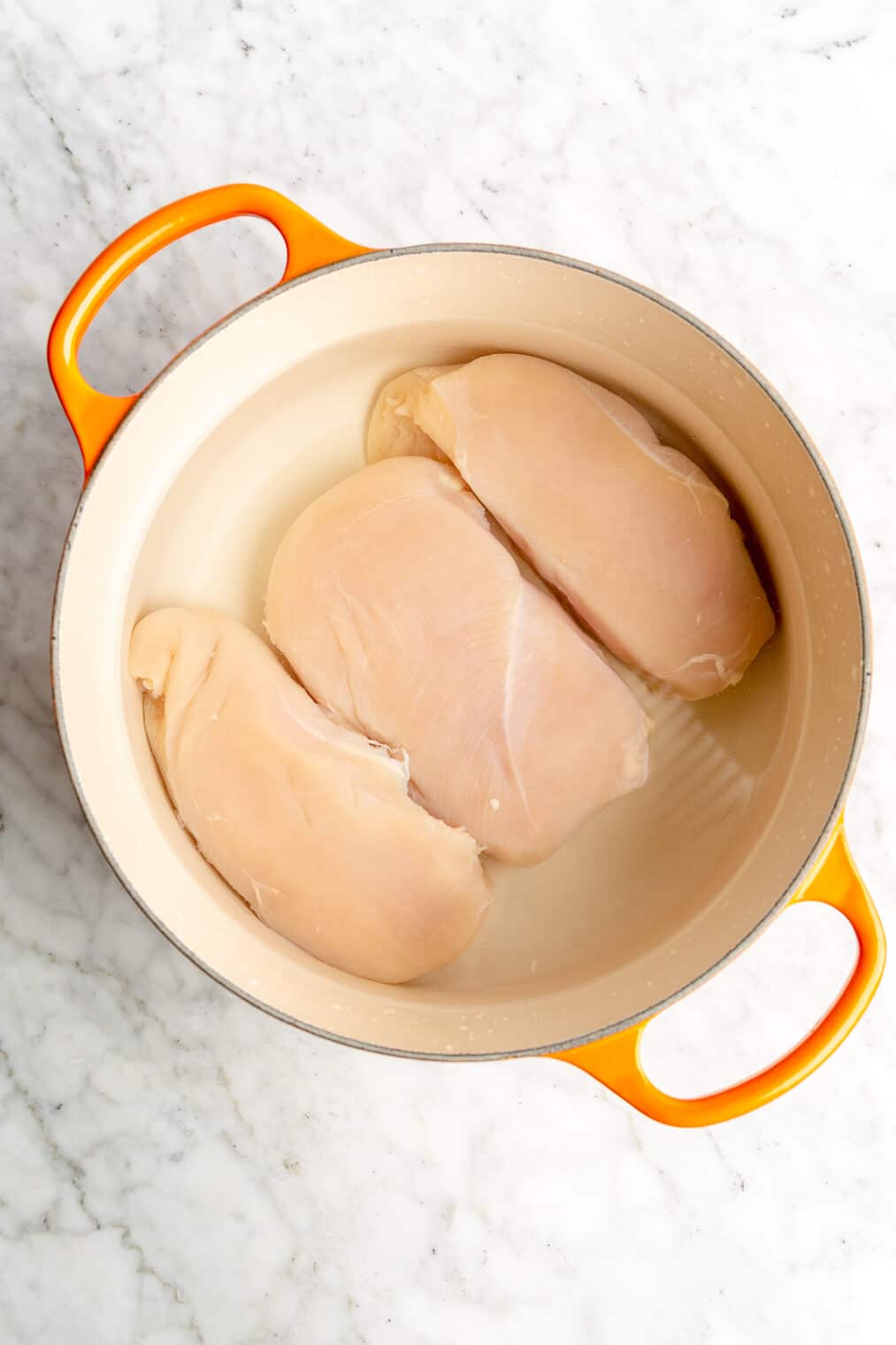 A pot with 3 chicken breasts submerged in water.