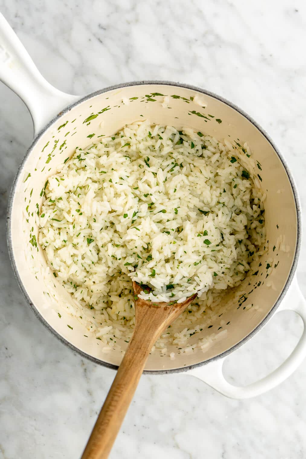 White rice with cilantro stirred into it in a white enameled cast iron pot.