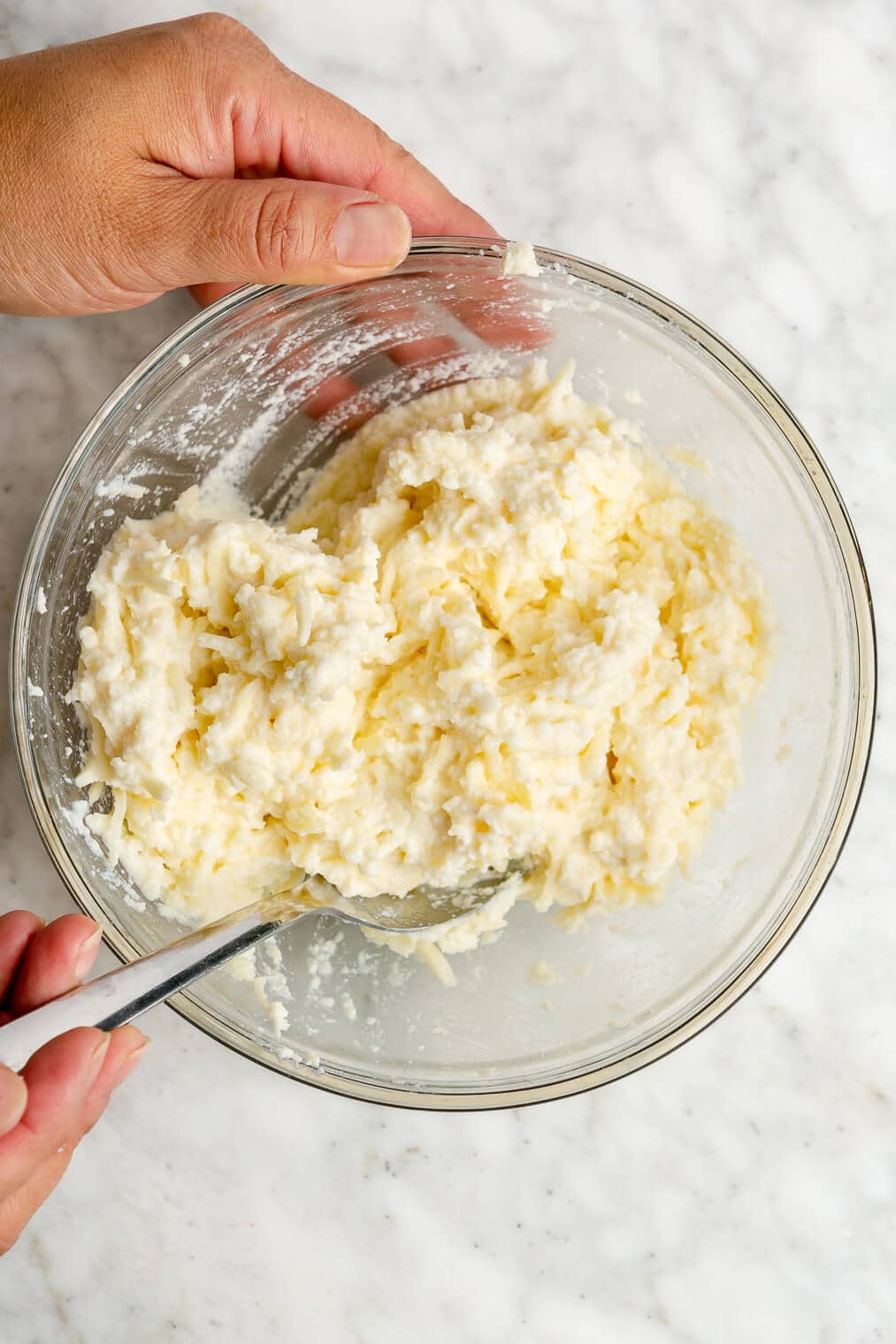 A person stirring together ricotta and mozzarella in a glass bowl.