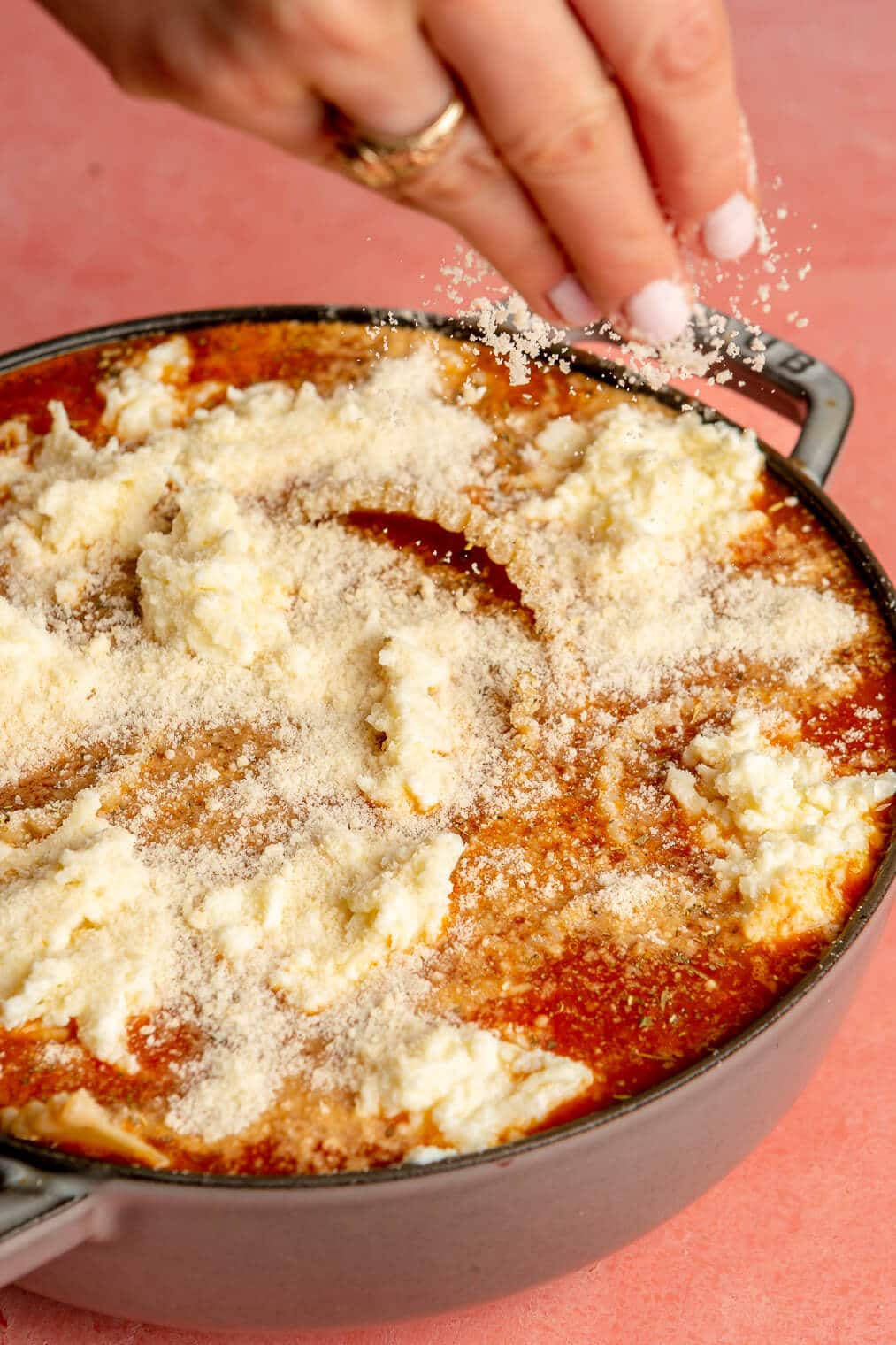A person sprinkling parmesan cheese over lasagna soup.