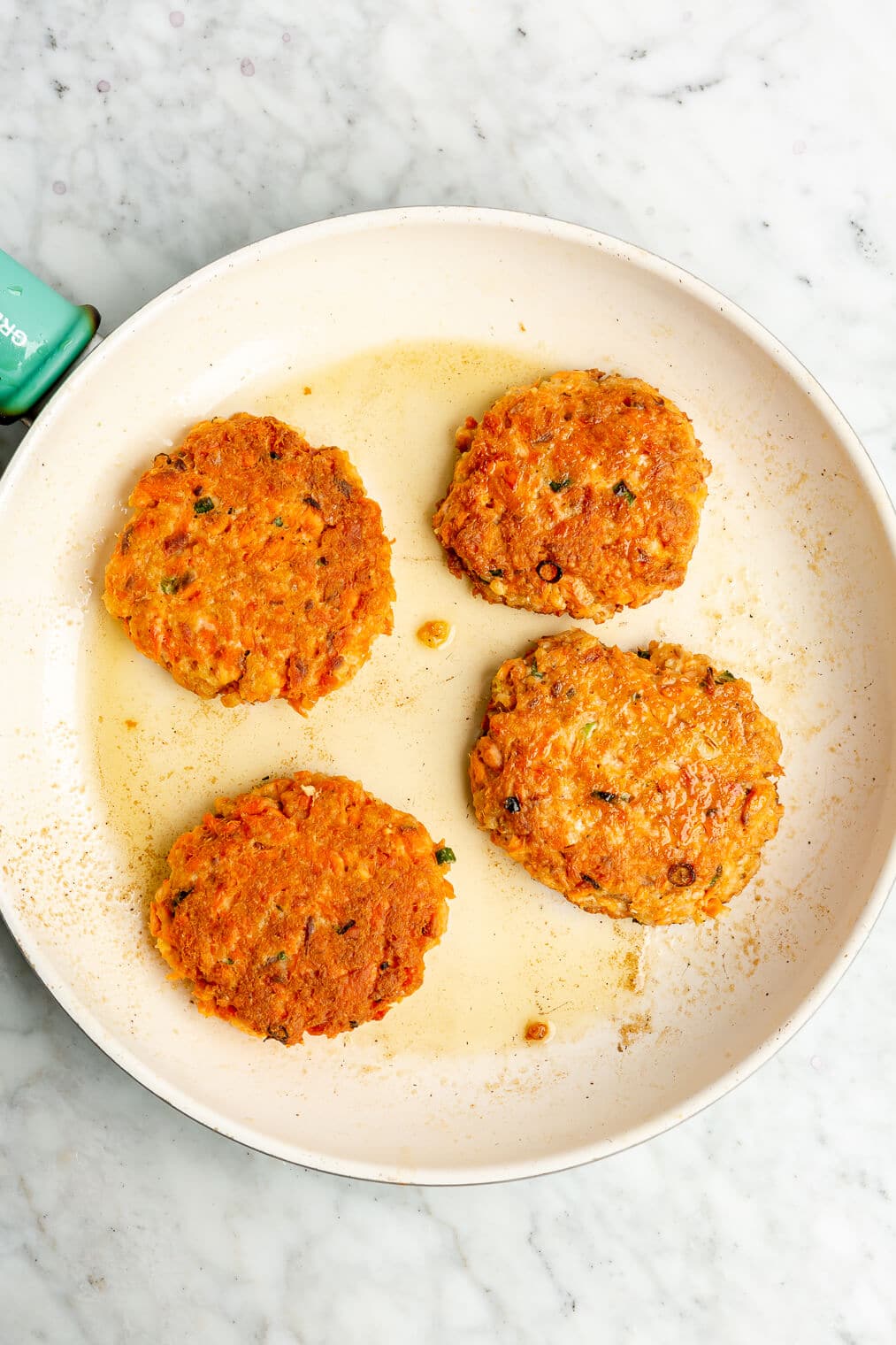4 salmon cakes cooking on a ceramic skillet.