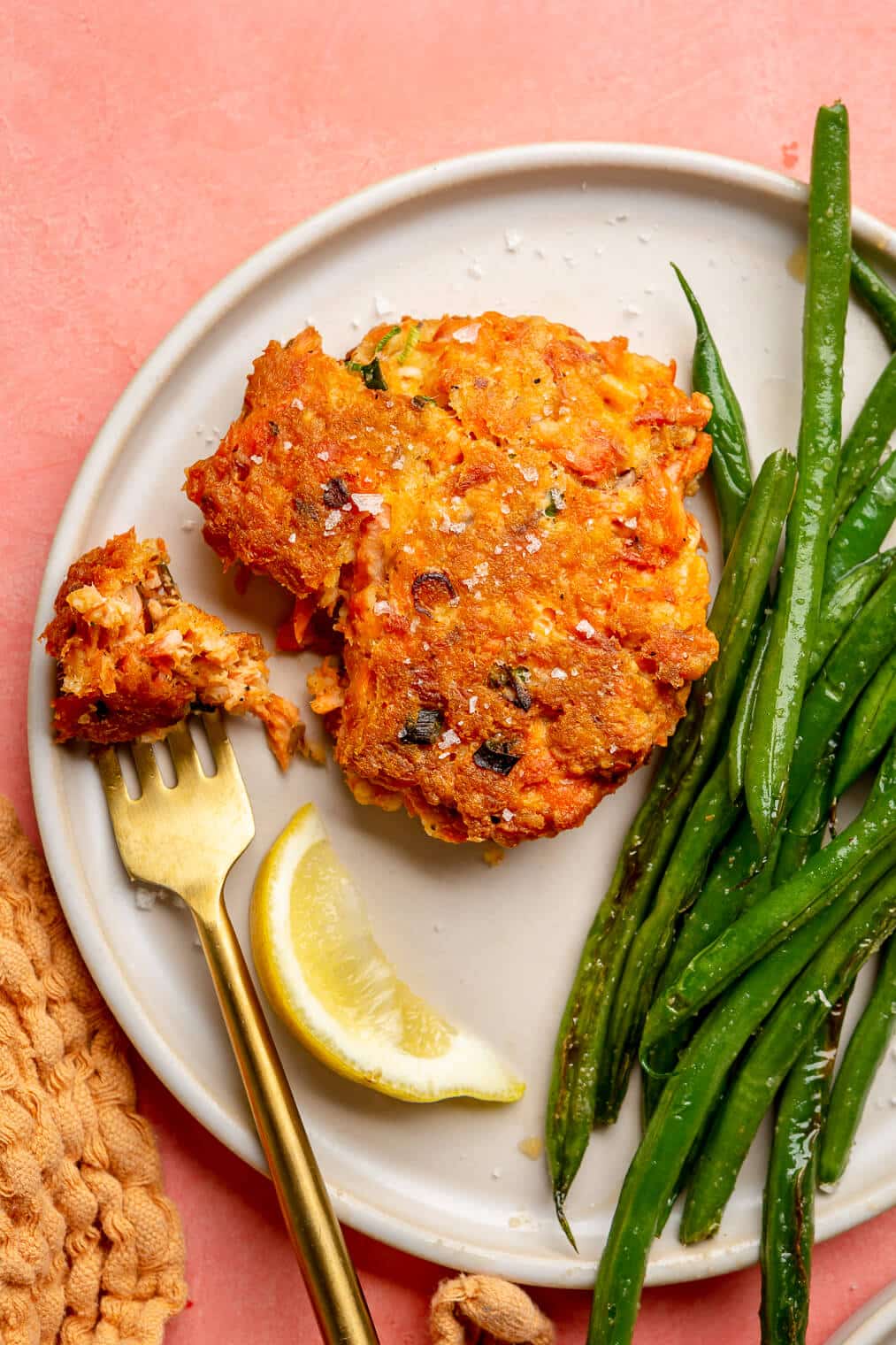 A salmon cake on a plate next to a lemon wedge and a serving of sauteed green beans.