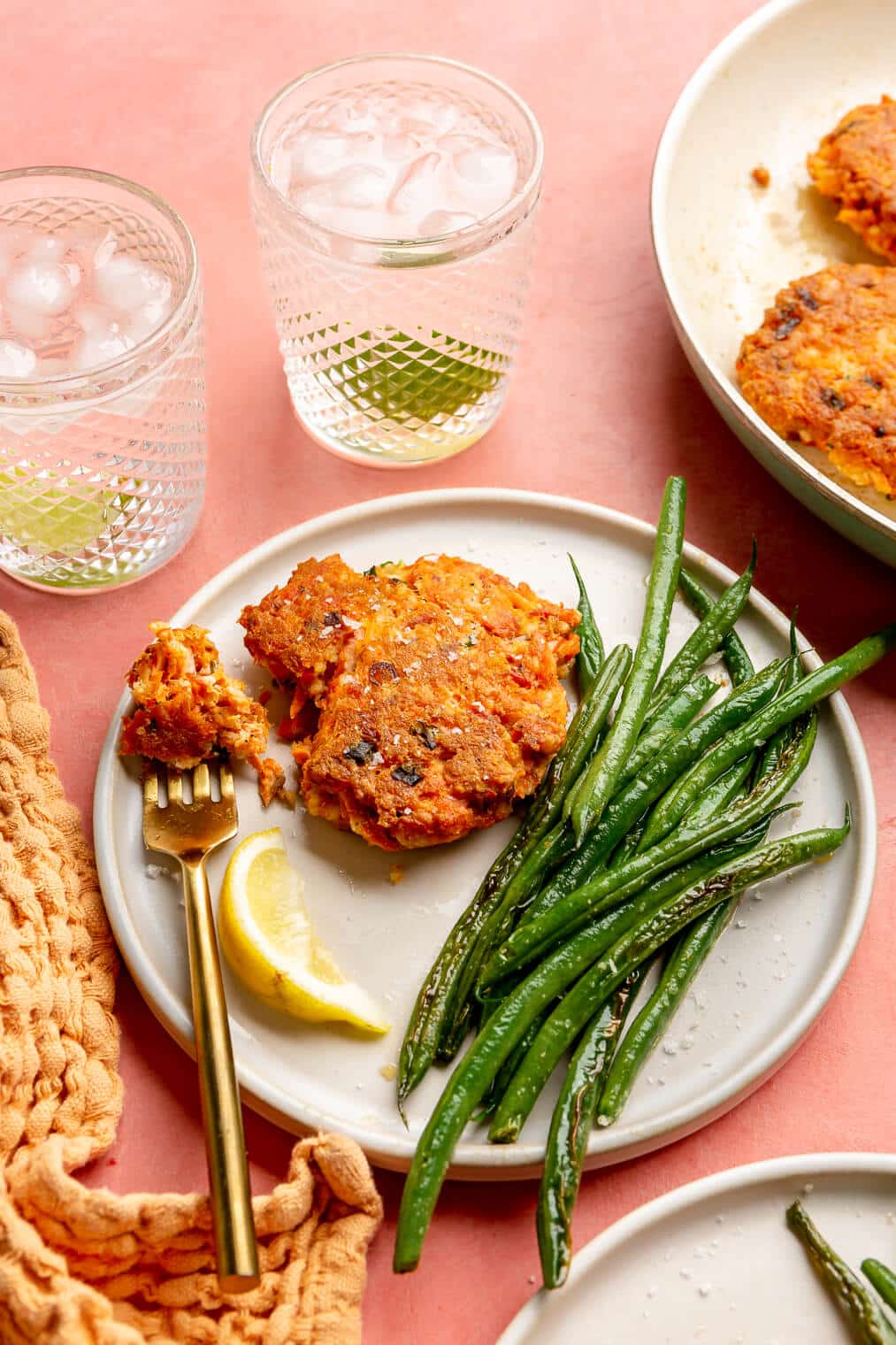 A salmon cake on a plate next to a lemon wedge and a serving of sauteed green beans.