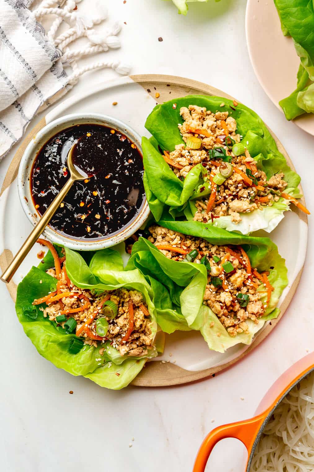 Three lettuce wraps on a plate with a bowl of dark, thick, sticky sauce.