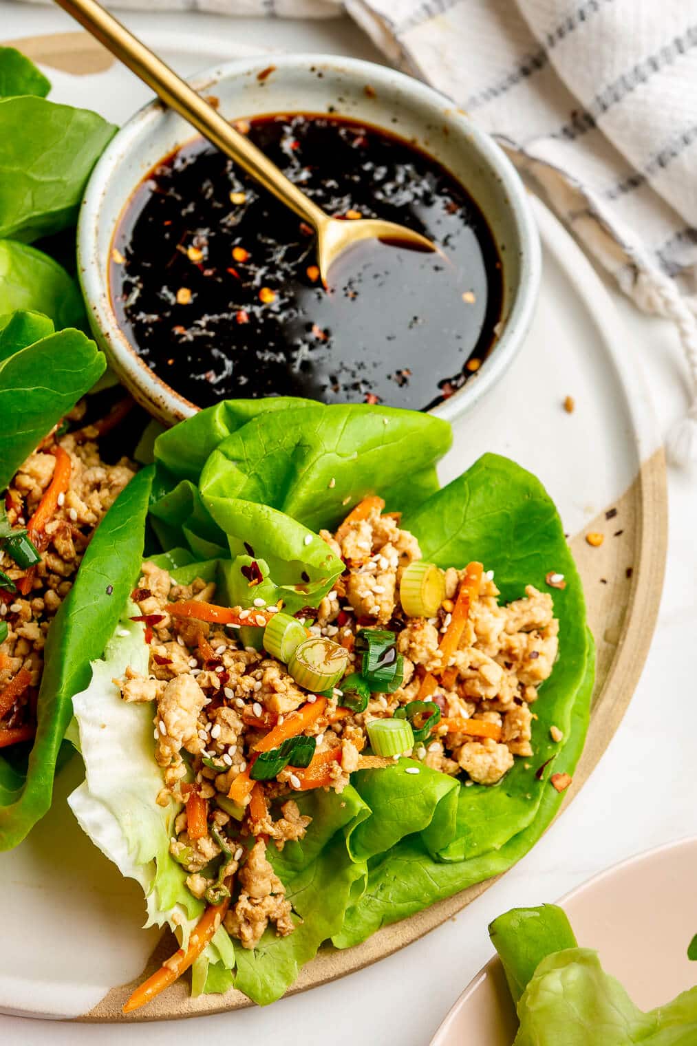 Three lettuce wraps on a plate with a bowl of dark, thick, sticky dipping sauce.