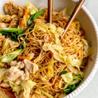 A white bowl of pancit with two wooden chopsticks.