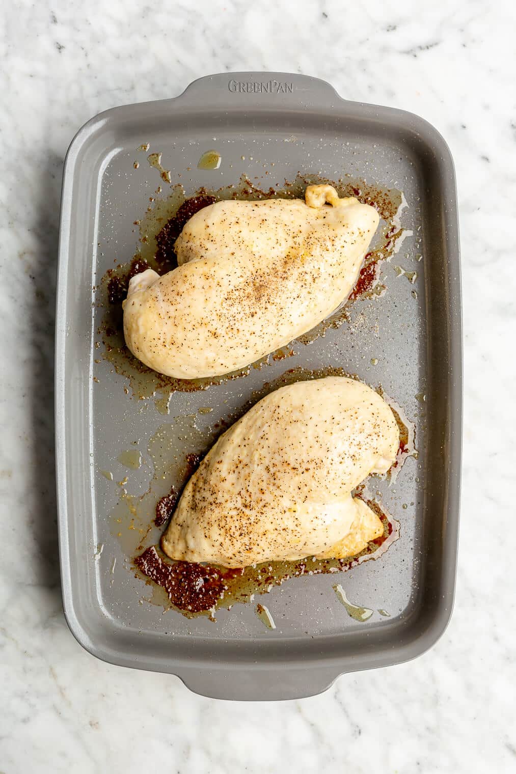 Two baked chicken breasts on a sheet pan.