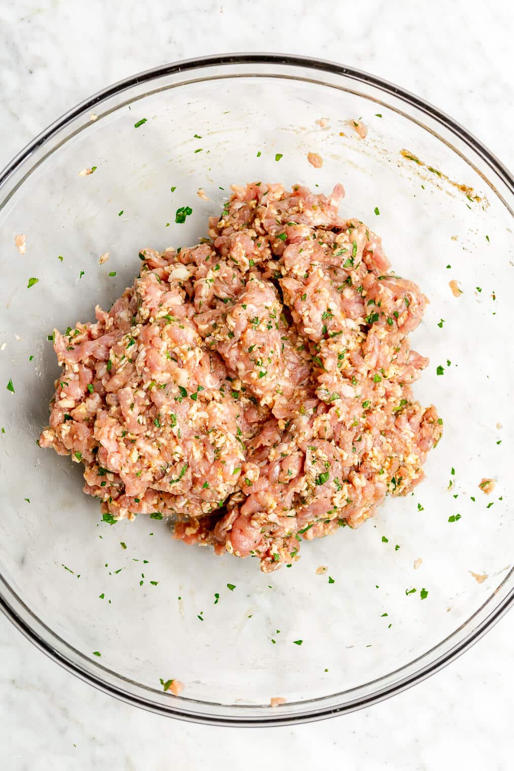 A large glass bowl with a raw Swedish meatball mixture in it.