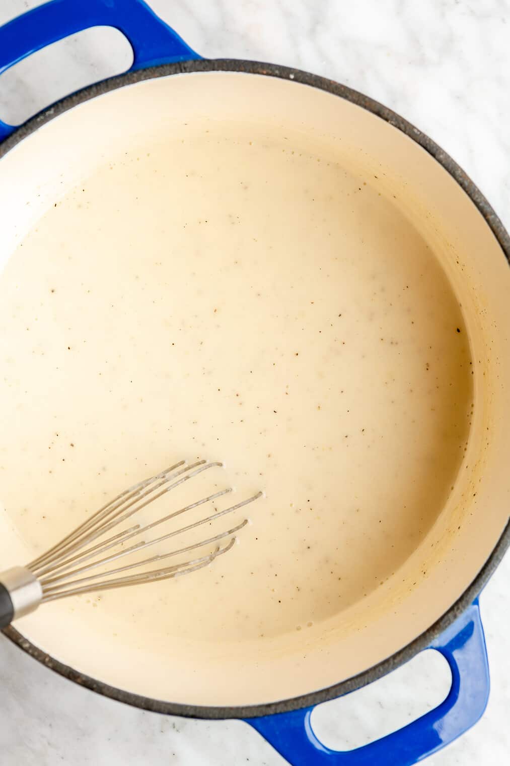 A whisk in a large enameled cast iron pot of white gravy.