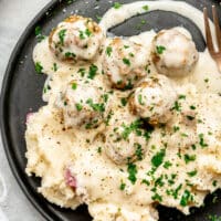 A plate of mashed potatoes and Swedish meatballs with gravy.