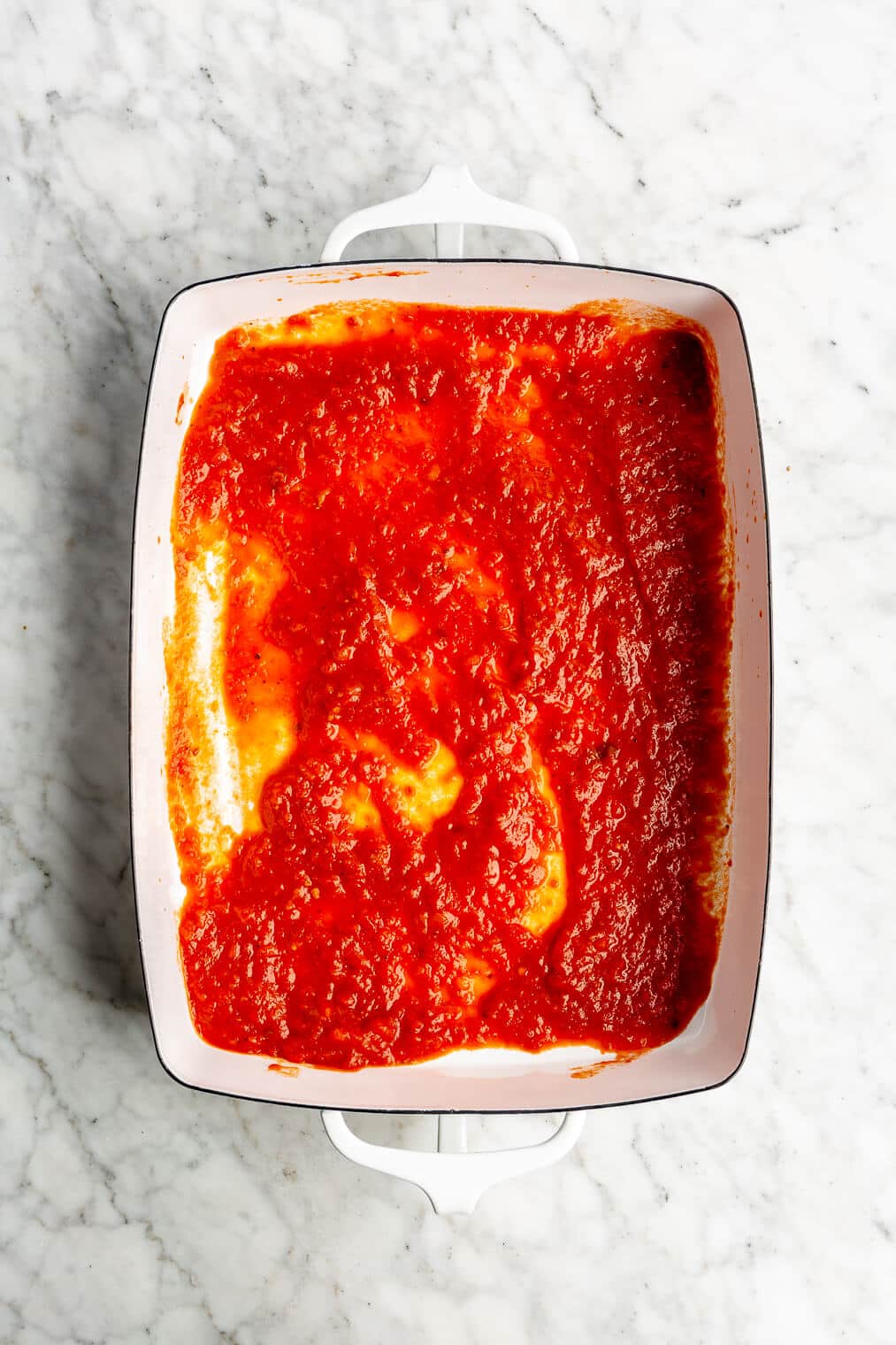 Top view of a casserole dish with marinara sauce spread in an even layer on the bottom.