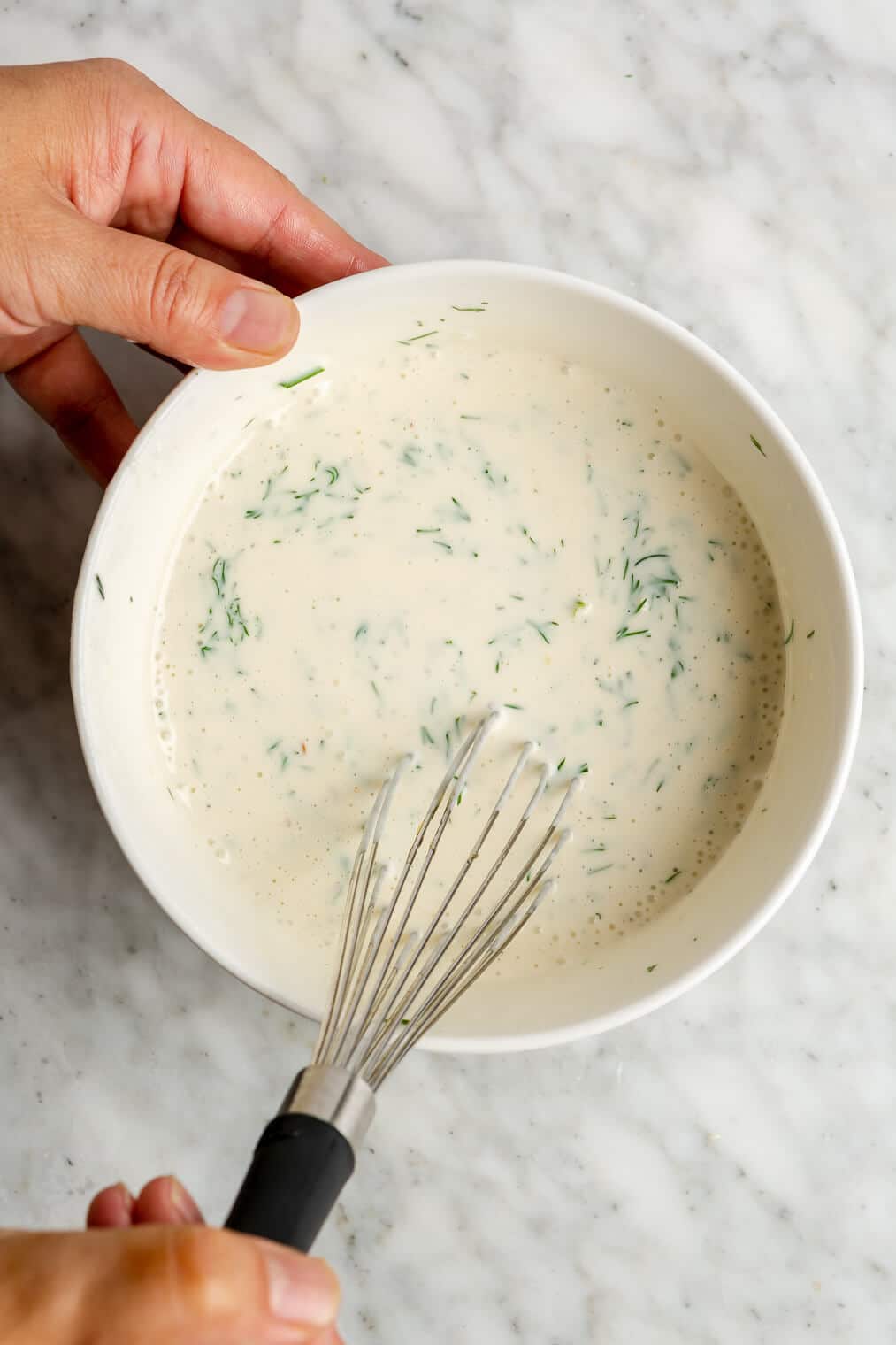 A person whisking together a creamy dressing for tuna pasta salad.