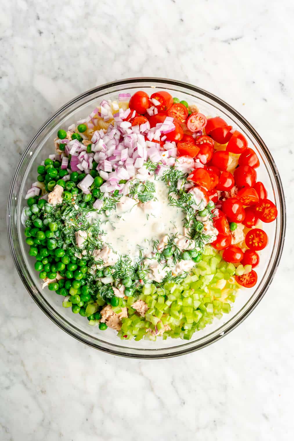 A top view of all of the ingredients for tuna pasta salad in a large glass bowl.