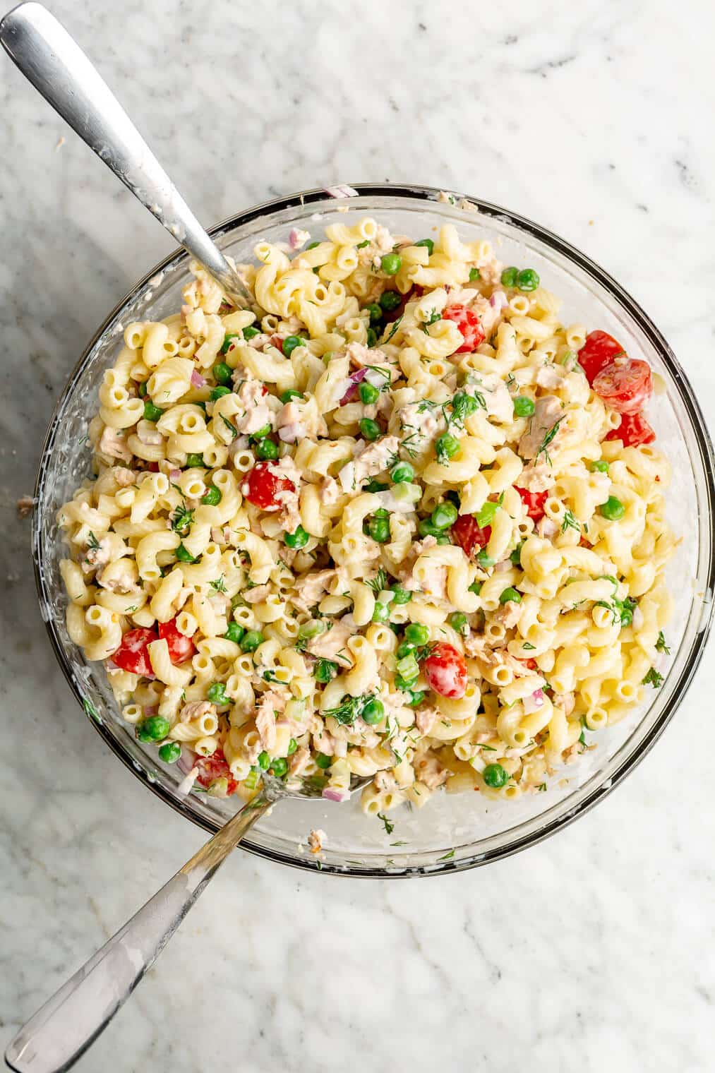 Two spoons in a large bowl of tuna pasta salad.