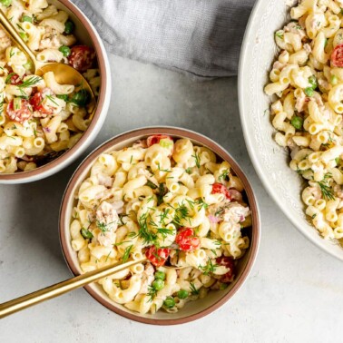 Top view of a large dish of creamy tuna pasta salad next to two servings of pasta salad in bowls.