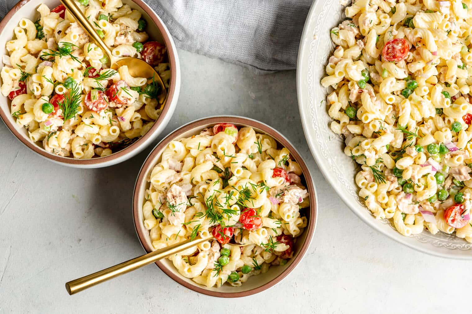 Top view of a large dish of creamy tuna pasta salad next to two servings of pasta salad in bowls.