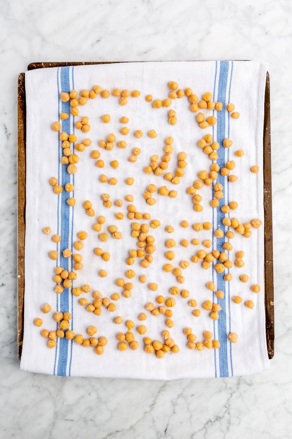 Raw chickpeas spread out on a dish towel lined sheet pan.