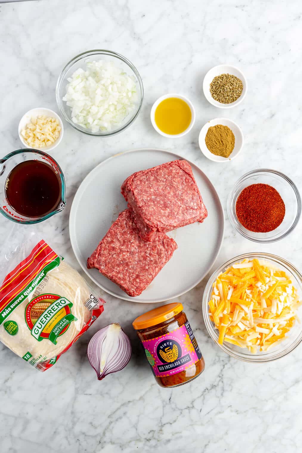 All of the ingredients needed for ground beef enchiladas on a marble surface.