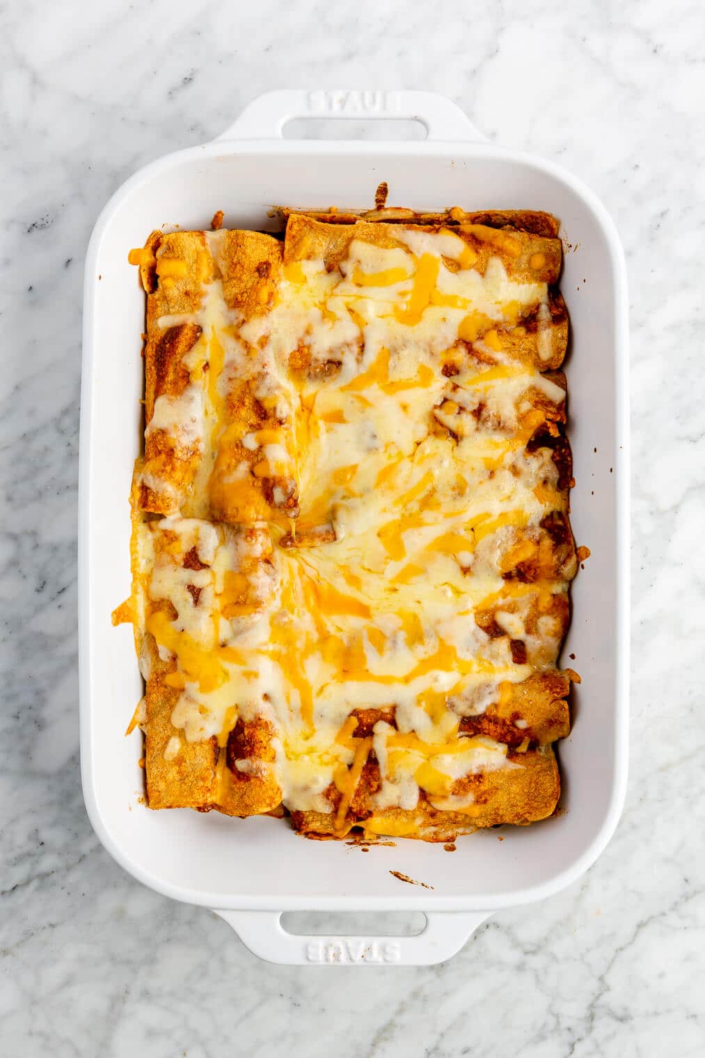 12 baked enchiladas topped with cheese in a casserole dish.