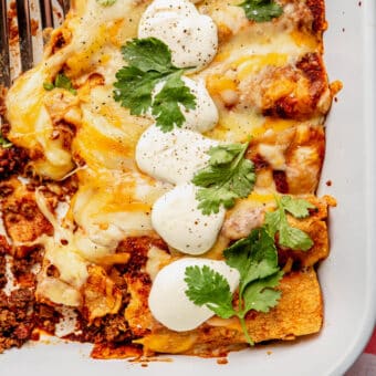A large casserole dish of ground beef enchiladas topped with sour cream and cilantro.