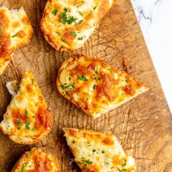 Cheesy garlic bread cut into pieces and sitting on a wooden cutting board.