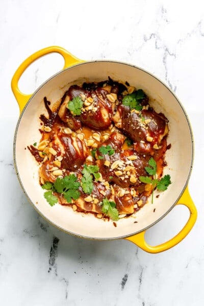 Chicken thighs topped with peanut sauce, cilantro, and peanuts in a large enameled cast iron pot.
