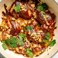 Chicken thighs topped with peanut sauce, cilantro, and peanuts in a large enameled cast iron pot.