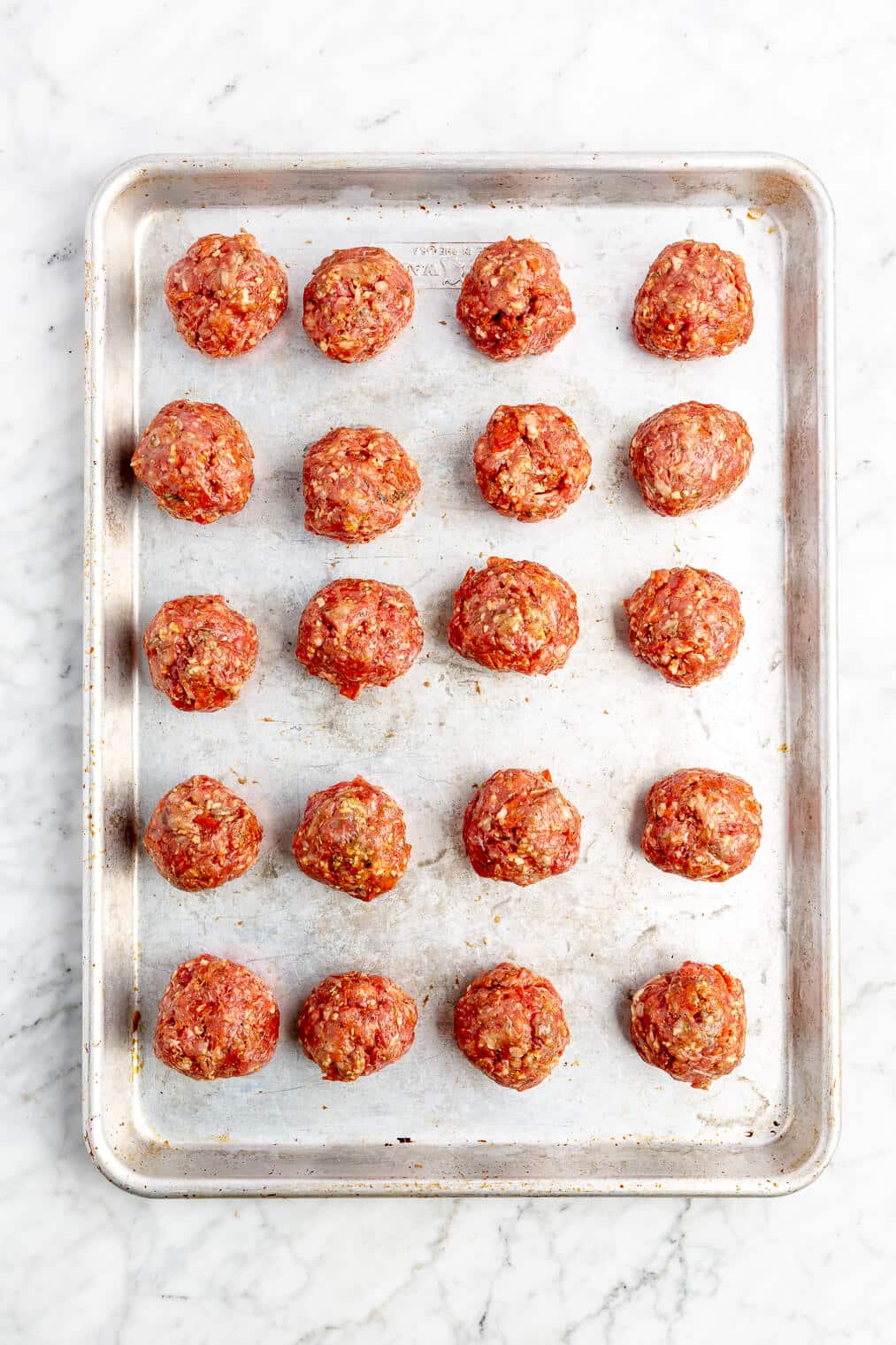 20 raw pizza meatballs in rows on a sheet pan.