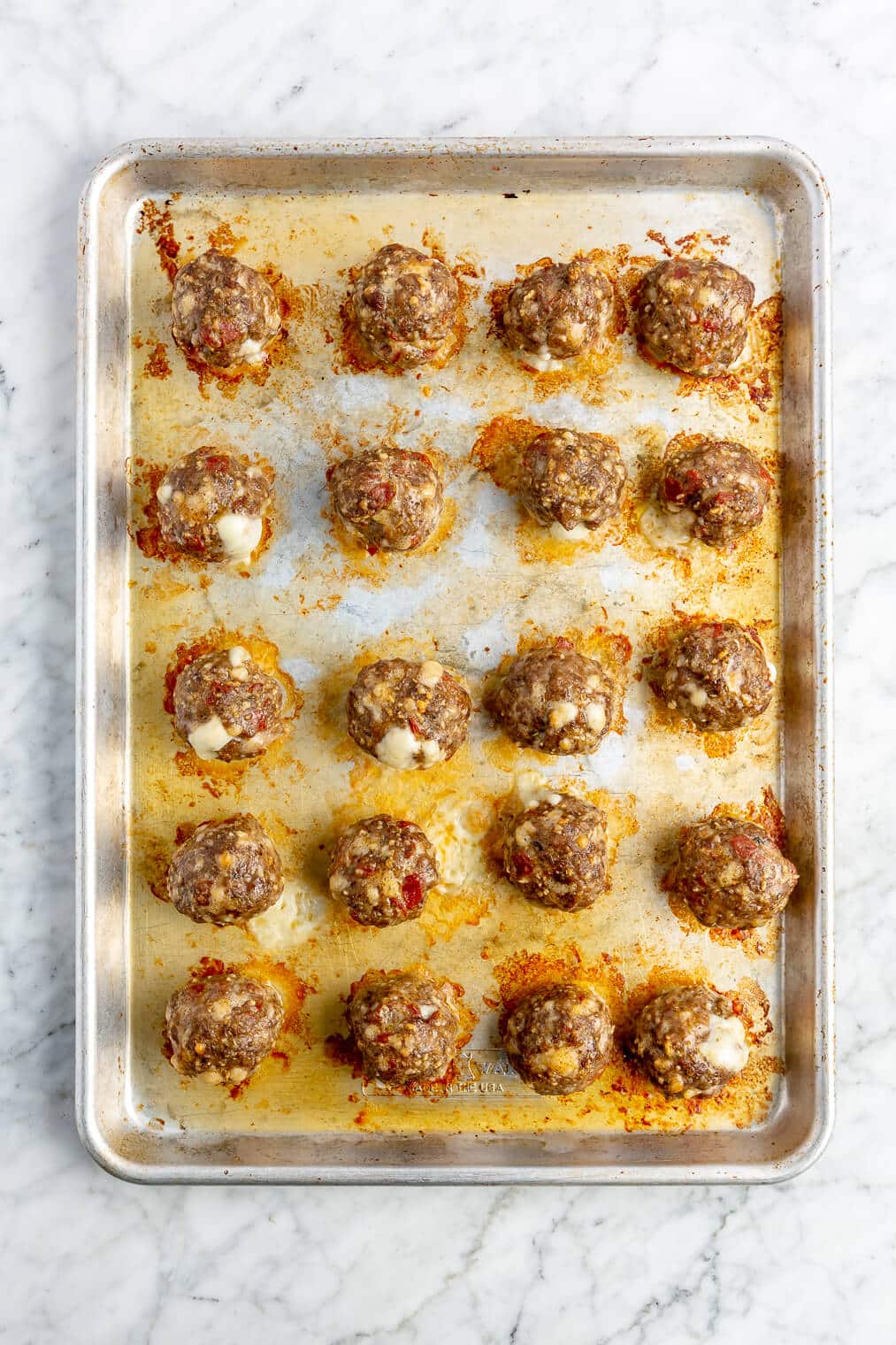 20 cooked pizza meatballs in rows on a sheet pan.