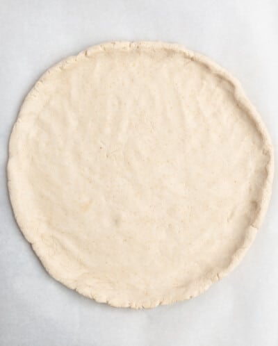 pizza dough spread out on parchment paper before being topped with pizza toppings
