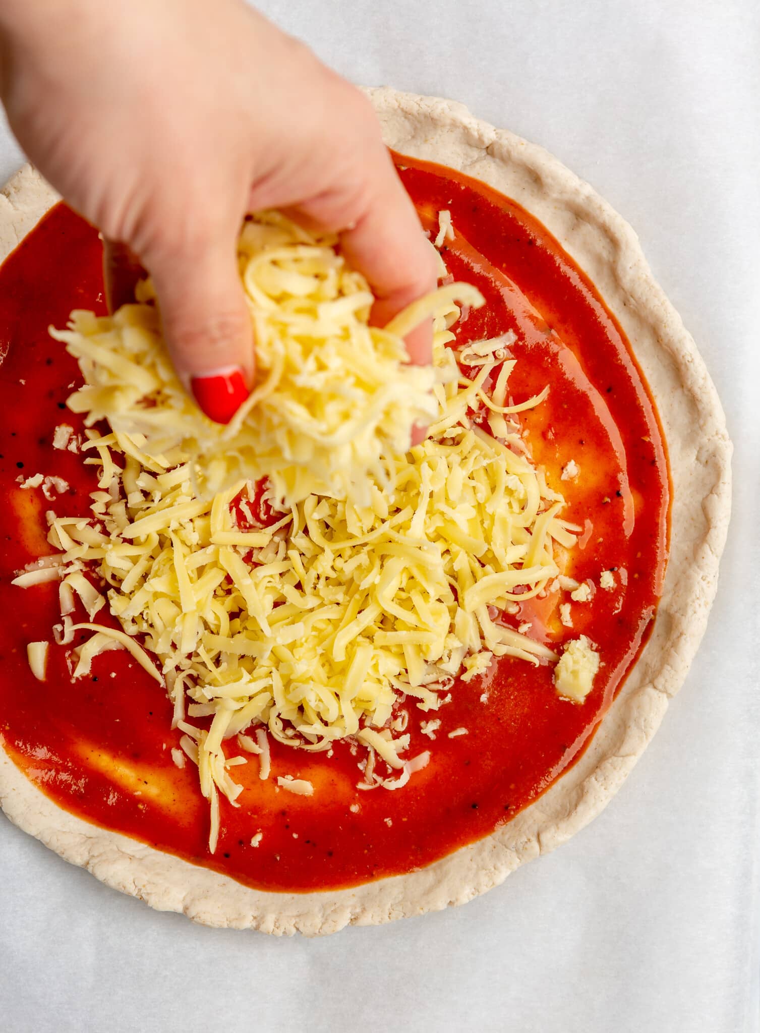 A person using their hands to sprinkle mozzarella cheese onto pizza dough.