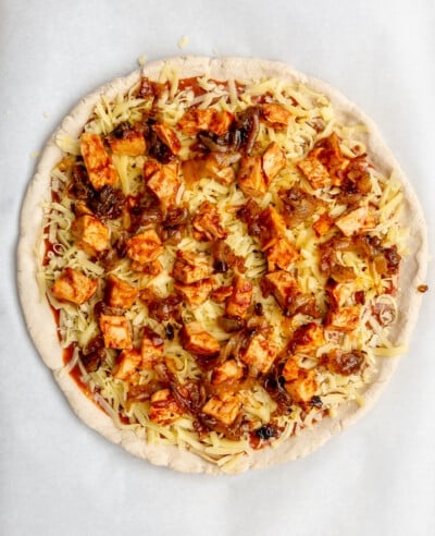 Raw pizza dough topped with BBQ sauce, BBQ chicken, caramelized onions, and mozzarella cheese.