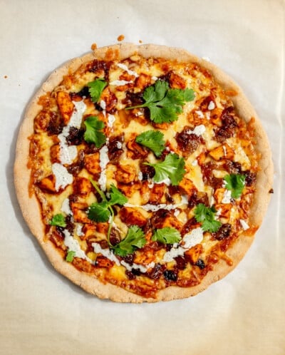 BBQ chicken pizza garnished with cilantro and ranch dressing before being cut.