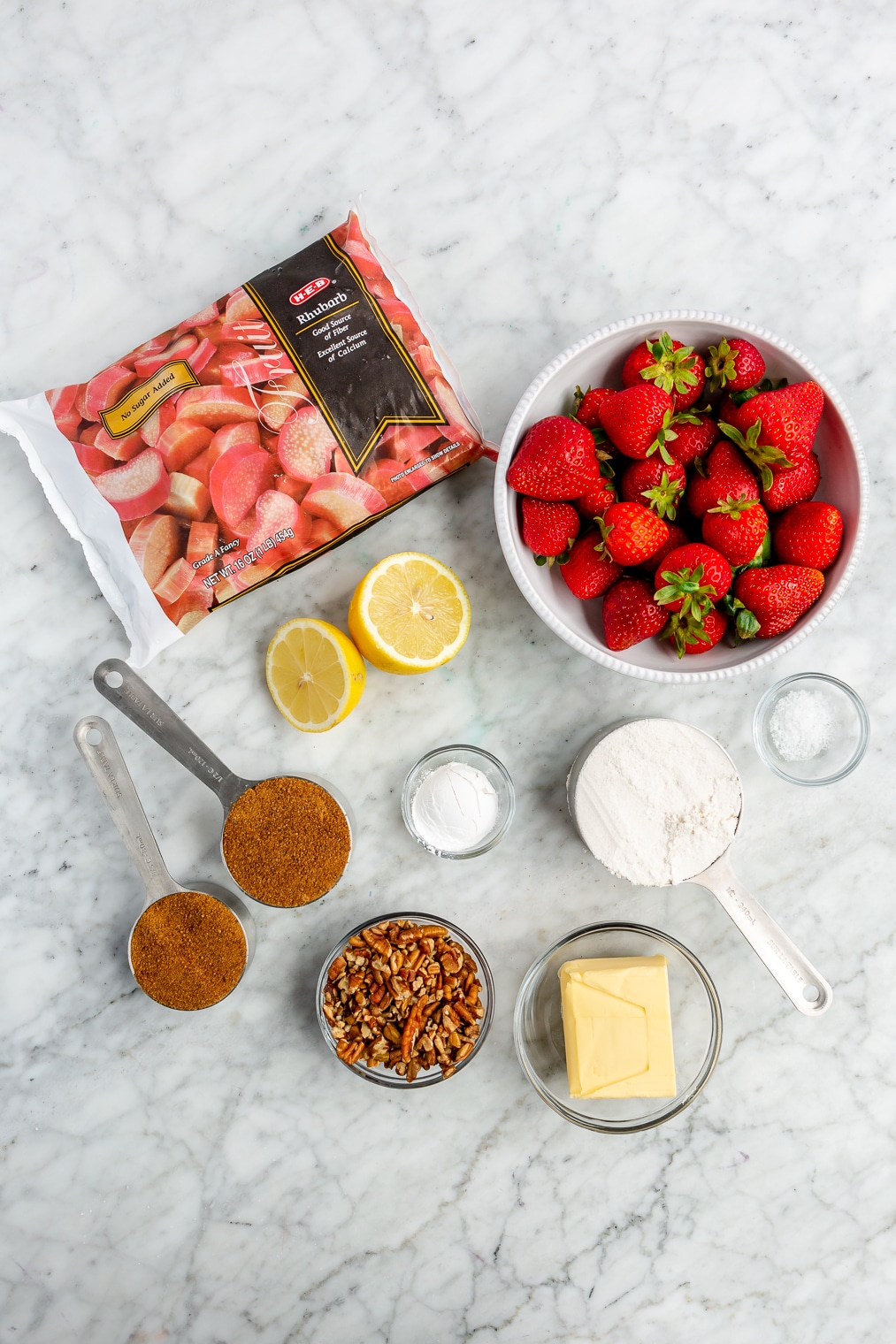 All of the ingredients for a strawberry rhubarb crisp on a marble surface.