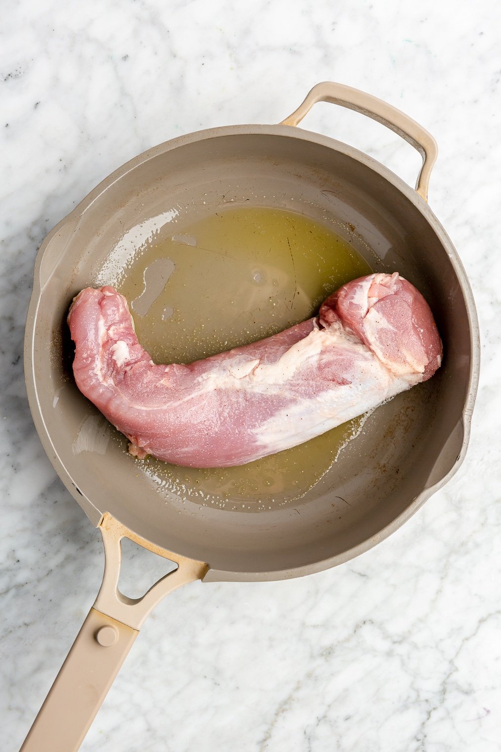 A raw pork tenderloin in a pan with oil.